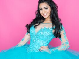 5 Tips for Planning the Perfect Winter Quinceañera A teenager with loosely curled hair stands with her hand on her hip, wearing a vibrant cyan ballgown with sheer sleeves.