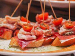5 Delicious, but Underrated Foodie Hotspots in Europe A plate of pintxos from San Sebastián, Spain. There are pieces of toasted bread with cured meats and a cherry tomato speared on top.