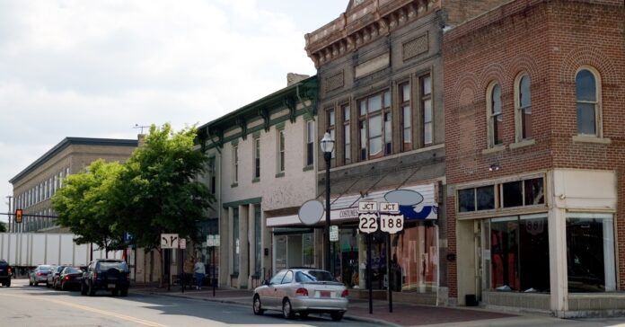A strip of old businesses in a small Midwestern downtown area. There are a few cars parked on the street.