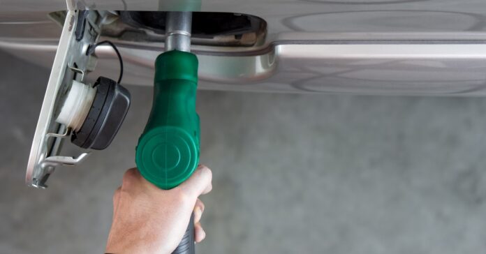 Overhead view of a green diesel nozzle inserted into the fuel filler neck of a gray vehicle, with a person's hand gripping the nozzle.