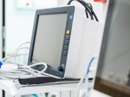 Two large pieces of medical equipment in a healthcare facility. Both machines have screens, and one has a white tray.