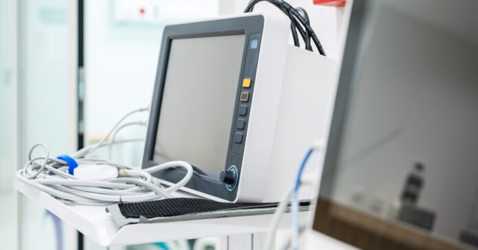 Two large pieces of medical equipment in a healthcare facility. Both machines have screens, and one has a white tray.