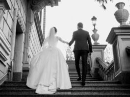 A bride and groom in a wedding dress and suit walk up elegantly crafted stairs on their wedding day.