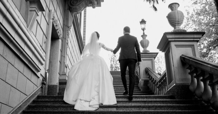 A bride and groom in a wedding dress and suit walk up elegantly crafted stairs on their wedding day.