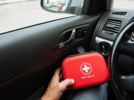 A view of a driver's hand as they hold a red container reading "First Aid Kit" while sitting in a car.