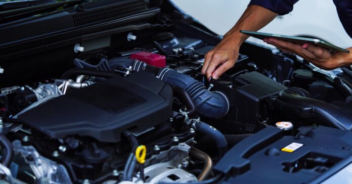 A person with their sleeves rolled up holding a tablet and using a small screwdriver to repair a car.