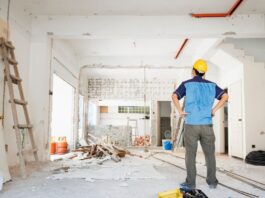 A man facing away from the camera with hands on hips looking at a home being remodeled with bare white walls.