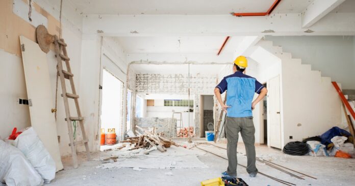 A man facing away from the camera with hands on hips looking at a home being remodeled with bare white walls.