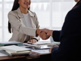 Tips for Choosing Your Suppliers as a Growing Business A woman in professional dress shakes the hand of a man on the other side of a table full of business documents.