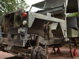 A classic Jeep with multiple missing tires, damaged paint, and a dirty windshield, placed on top of small metal poles.