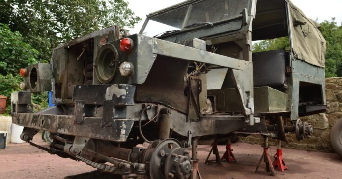 A classic Jeep with multiple missing tires, damaged paint, and a dirty windshield, placed on top of small metal poles.