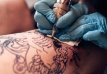 How to Make Your First Year as a Tattoo Artist Successful A person who is wearing blue gloves is holding a tattooing needle and is using it one another person.