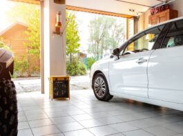A white car sits in an open double garage, on top of white tiles. Beside the white car is a black ATV.