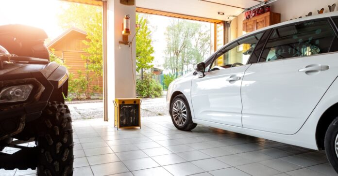 A white car sits in an open double garage, on top of white tiles. Beside the white car is a black ATV.