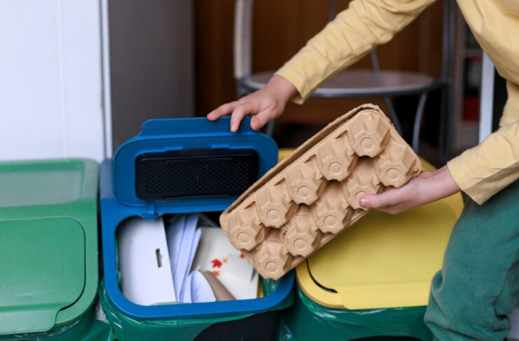 A person leaning in to throw something into the recycling bin. The bins have yellow, blue, and green lids.