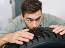 A man examining a brand-new tire. He has both hands on the top of the tire and is looking very closely at the tread.