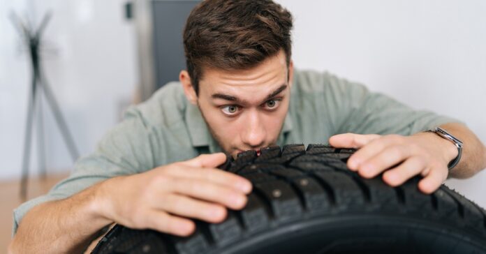 A man examining a brand-new tire. He has both hands on the top of the tire and is looking very closely at the tread.