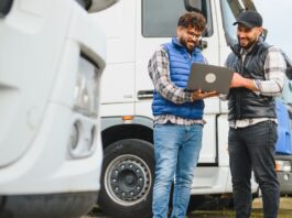 Truck drivers plan routes and logistics on a laptop beside a semi-trailer, coordinating a smooth, on-time delivery.