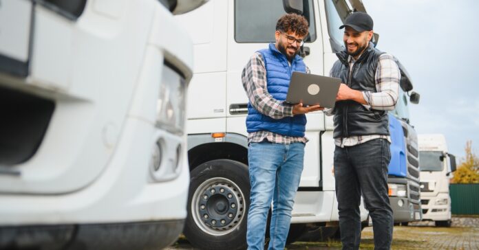 Truck drivers plan routes and logistics on a laptop beside a semi-trailer, coordinating a smooth, on-time delivery.