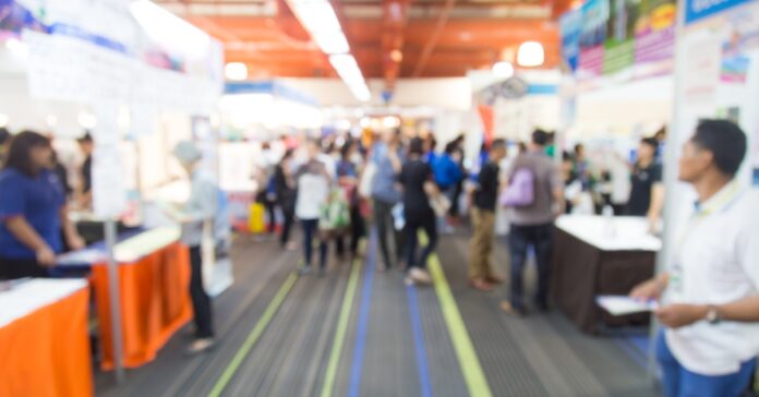 A blurred point-of-view of a person walking down the carpeted alleyway of a trade show with displays on both sides.