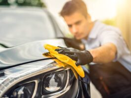A car detailer running a yellow microfiber towel along the headlight of a car that was just detailed.
