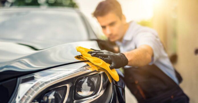 A car detailer running a yellow microfiber towel along the headlight of a car that was just detailed.