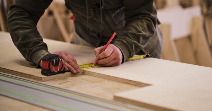 A carpenter measuring wood at a workbench using a measuring tape, capturing a precise moment in furniture making.