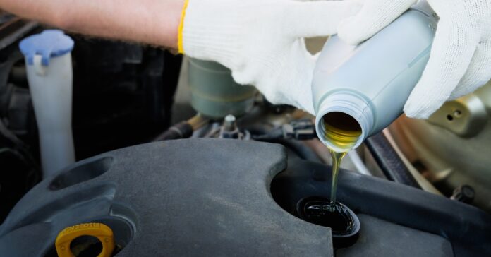 In a close-up, a person wearing white gloves pours oil into an engine opening surrounded by other car parts.