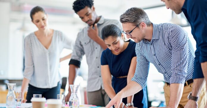 Team of diverse professionals collaborating around a table reviewing documents and ideas in an office workspace,