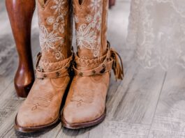 5 Signs a Western-Themed Wedding Is Right for You A pair of boots placed together beneath a wedding dress with lace fabric draped above and details of the footwear visible.