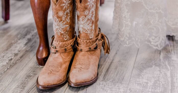 A pair of boots placed together beneath a wedding dress with lace fabric draped above and details of the footwear visible.