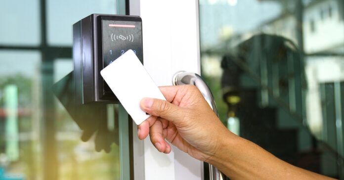 A close-up view shows a person holding up a blank, white card up to an access control machine that's next to a glass door.