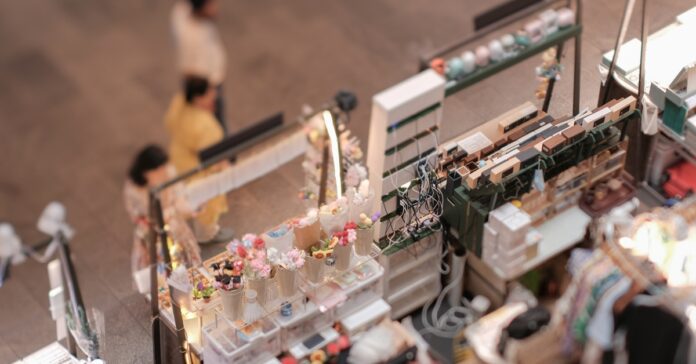 An aerial view shows a booth selling jewelry at a pop-up event. Three people are walking in front of it.