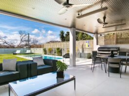An outdoor living space with a swimming pool, trampoline, and covered outdoor kitchen with a dining table and additional seating.