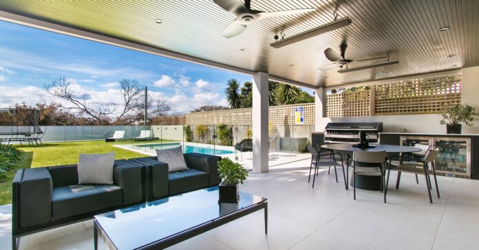 An outdoor living space with a swimming pool, trampoline, and covered outdoor kitchen with a dining table and additional seating.