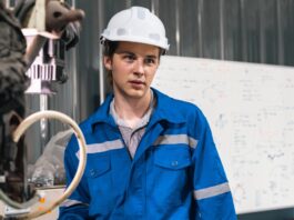 Two engineers wearing blue outfits looking at a large machine in a brightly lit industrial workplace.