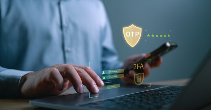 A person sits at a desk and uses the mousepad of a laptop. Security shield graphics hover above the keyboard.
