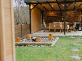 An outdoor living space with a fire pit and a covered area containing an outdoor kitchen setup and a table with chairs.