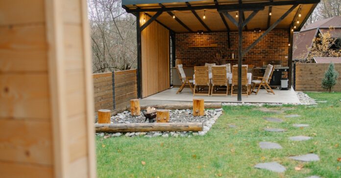 An outdoor living space with a fire pit and a covered area containing an outdoor kitchen setup and a table with chairs.
