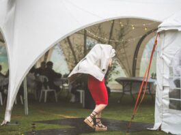How To Prepare for Windy Weather During Outdoor Events A guest at an event covering themselves with a jacket running to a large white tent. The weather is rainy and windy.