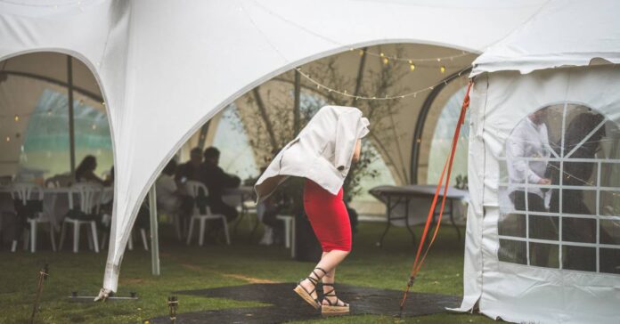 A guest at an event covering themselves with a jacket running to a large white tent. The weather is rainy and windy.