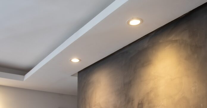 Two bright, recessed LED ceiling lights installed near a black wall and a doorway inside a large home.