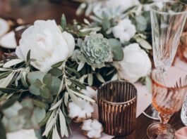 Wedding table set with white blooms, eucalyptus, succulents, crystal glasses, candles, and soft pink linens.