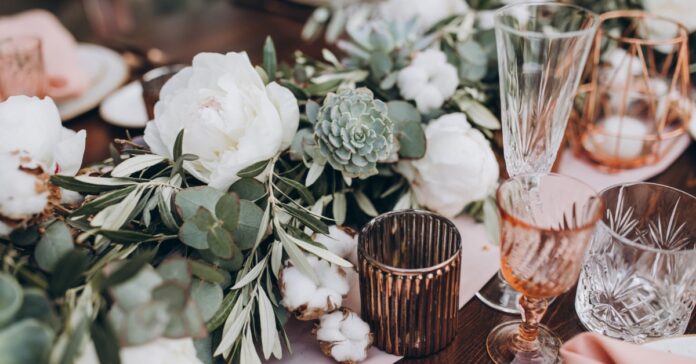 Wedding table set with white blooms, eucalyptus, succulents, crystal glasses, candles, and soft pink linens.