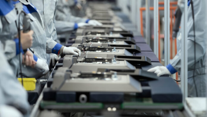 Workers assemble electronic devices on a manufacturing line while wearing protective clothing and gloves.