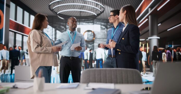 A group of business professionals stands together in a hallway while talking and holding papers during an event.