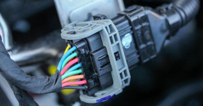A close-up of colored electrical wires connected to a black and gray plug inside a vehicle engine bay.