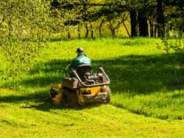 How To Extend the Working Life of Your Riding Mower A person driving a yellow riding lawn mower across a large, sunny green lawn surrounded by leafy trees.