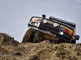 Turn Your Ford Bronco Into an Unstoppable Off-Road Vehicle A yellow Bronco with metal protection and bar lights on top, climbing a small hill through a dirt road covered in mud.
