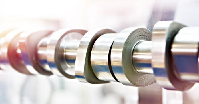 A close-up view shows a camshaft that is made of metal. The background is incredibly blurry and illuminated.